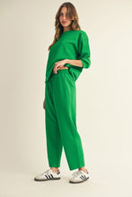 Load image into Gallery viewer, Woman wearing a green outfit with wide-leg pants and a matching top on a beige background