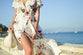 Woman wearing floral white summer dress and bag on the sea shore