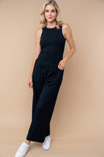 Load image into Gallery viewer, Woman wearing a black sleeveless top and wide-leg pants against a beige background
