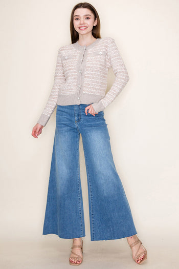 Woman wearing a light gray cardigan and blue jeans on a plain background