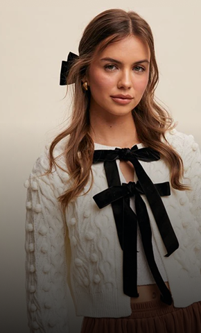Woman wearing a white blouse with black ribbons against a beige background
