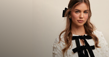 Woman with long hair wearing a black bow in her hair against a beige background