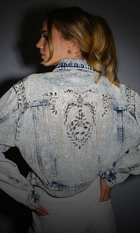 Person wearing a light blue denim jacket with intricate patterns on a dark background