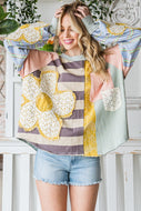 A woman wearing a pink long-sleeved cotton top with multi fabric patches including a daisy design, a round neckline, and raw edge details.